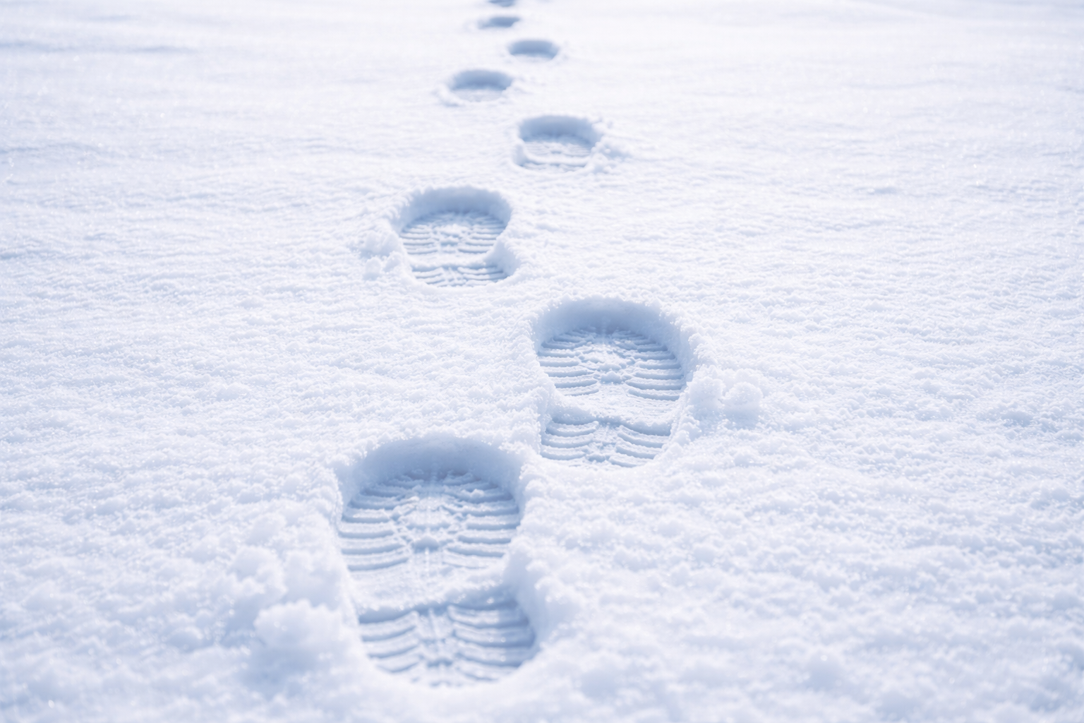 Footprints in fresh snow forming a straight path into the distance